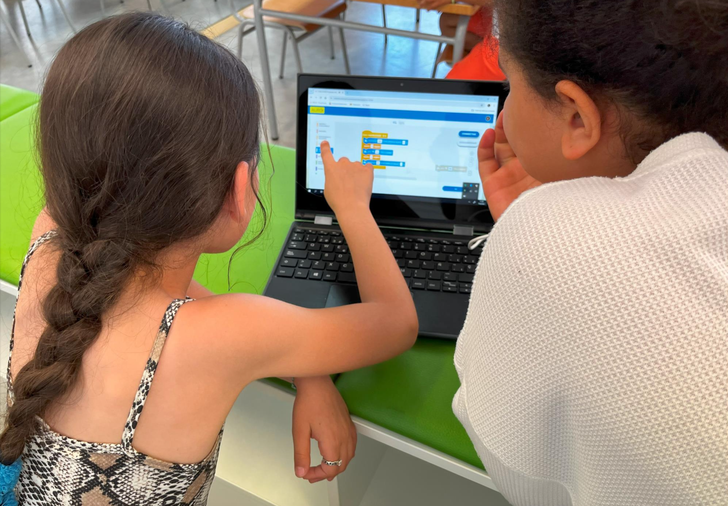 Two girls from behind looking at a laptop. One of them is pointing someout on the screen.